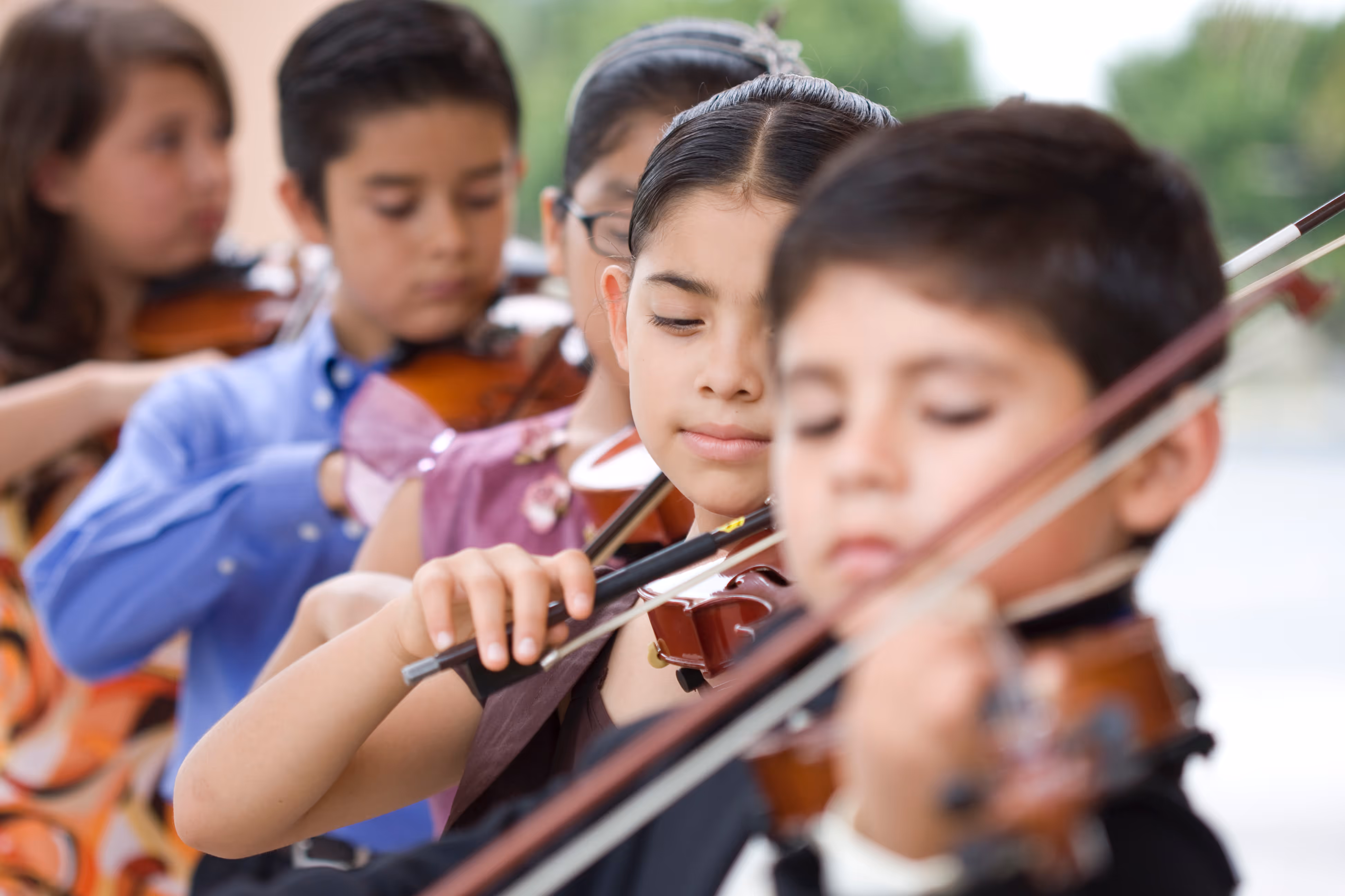 Group of children playing violins in an outdoor setting.